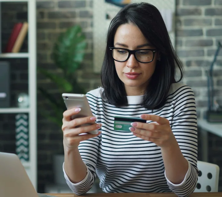 A woman holding a phone in one hand and a credit card in the other.