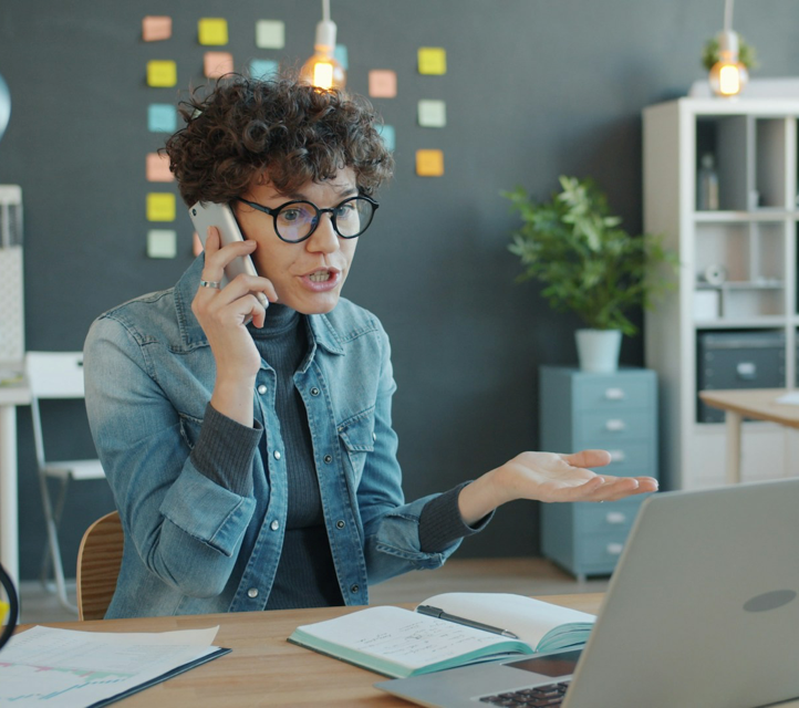 A frustrated-looking woman on the phone in front of a laptop.