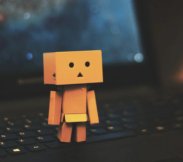 A cardboard robot standing on the keyboard of a laptop.