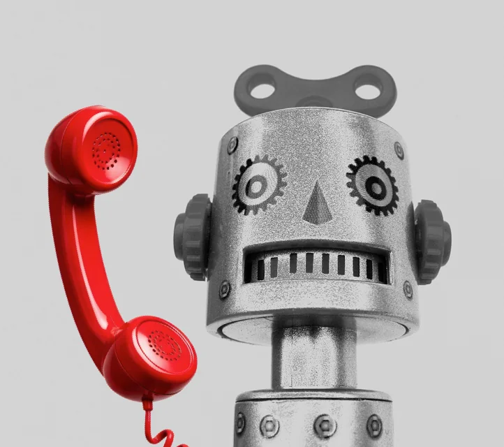 A toy robot with a red, 20th-century-style telephone handset next to its head.