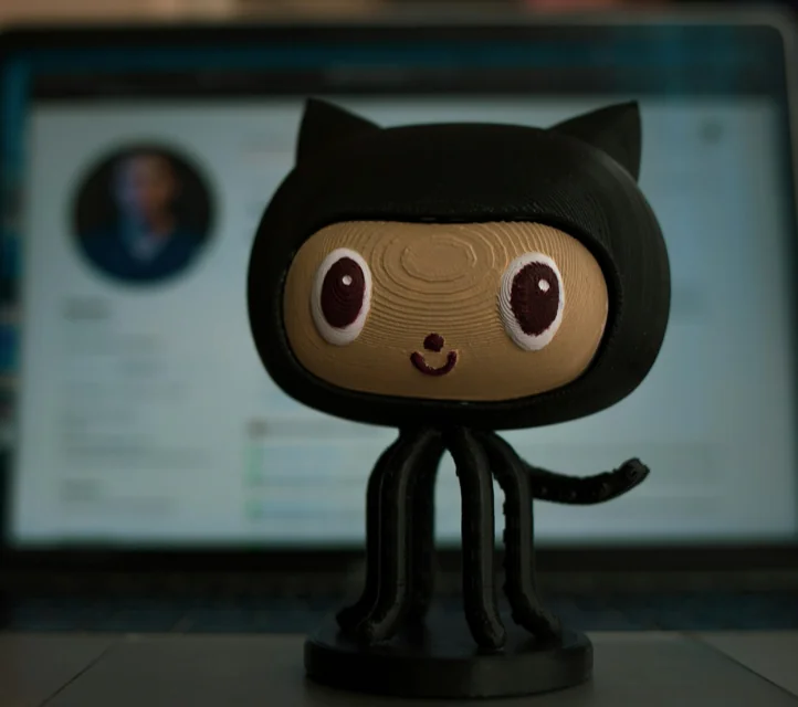 A wooden figurine of the GitHub Octocat with a computer screen in the background.