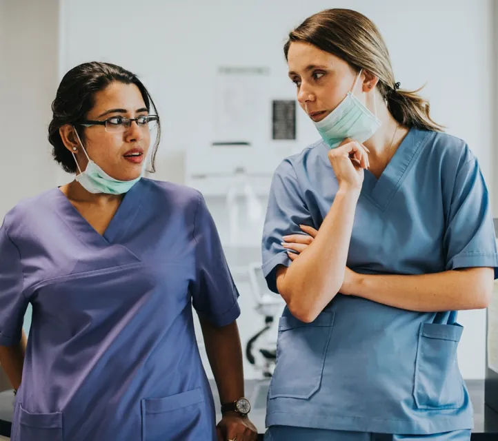 Two medical professionals side by side looking at each other as if they are suspicious of something.