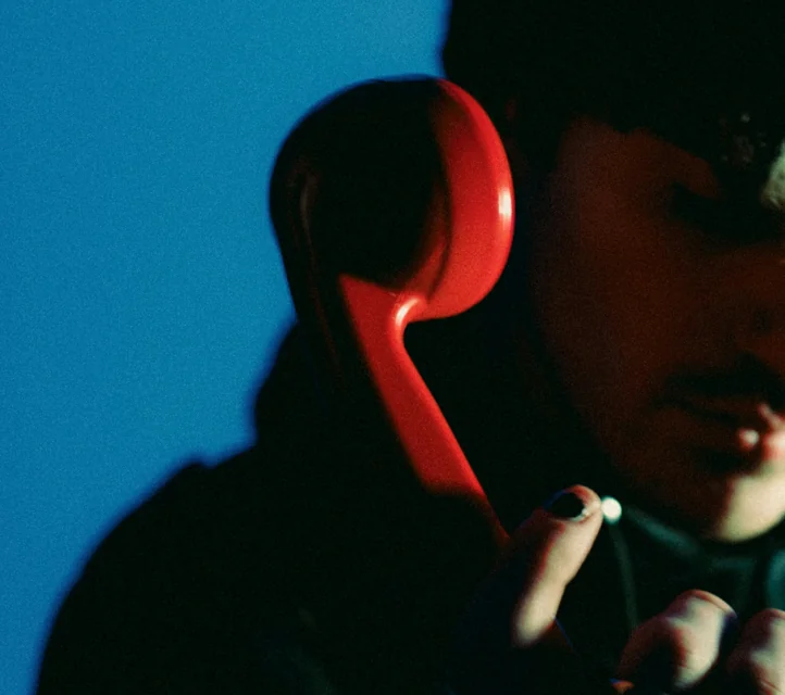 Closeup on a mysterious person with a shadowed face on a call with a red handset.
