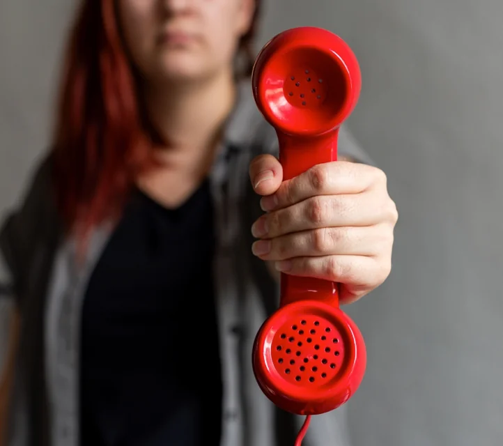 A woman holding out a red telephone receiver.