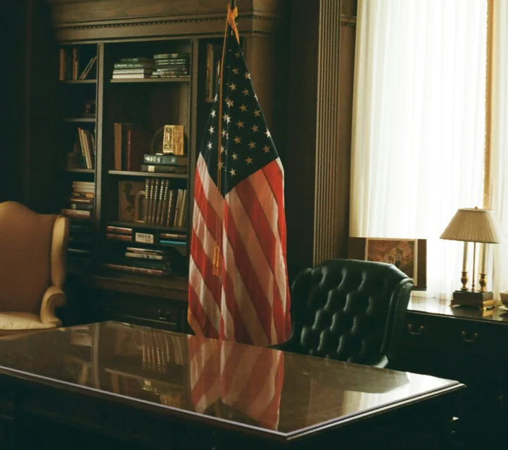 An office desk with an empty leather chair and an American flag behind it.